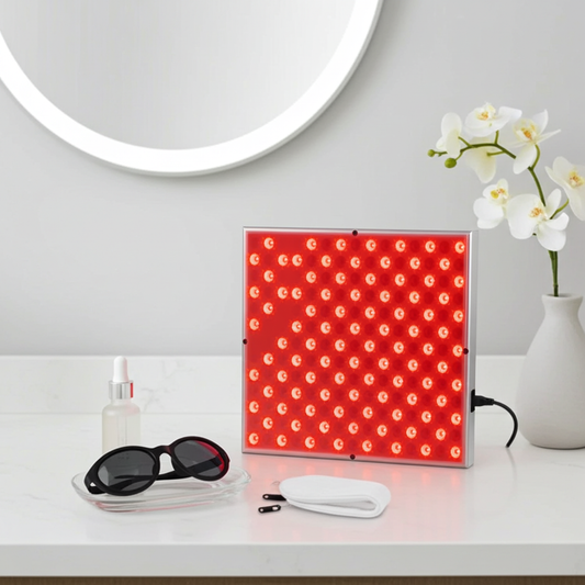 LED Red Light Therapy Panel Lamp lit up on white vanity with protective goggles, facial serum and white orchid – 660nm and 850nm dual wavelength red light therapy for facial anti-ageing and skin care
