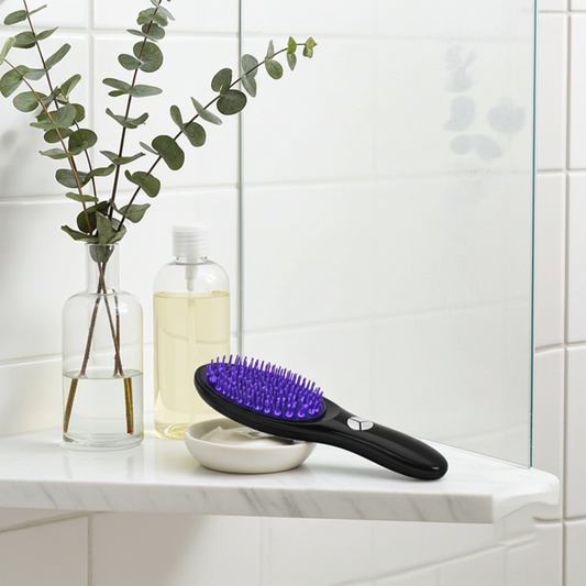 Electric Scalp Massager and Hair Growth Comb on wooden surface with green leaves and eucalyptus – blue LED light therapy comb for hair growth and scalp stimulation